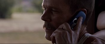 Movie still from “Cop Car” (2015), directed by Jon Watts – A person talking on a cell phone; Close Up shot, Over the shoulder angle