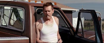 Movie still from “Cop Car” (2015), directed by Jon Watts – A man smoking a cigarette while standing in the back of a truck; Medium shot, Over the shoulder angle