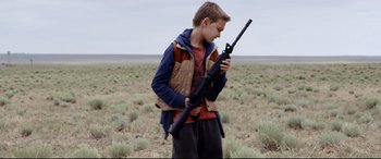Movie still from “Cop Car” (2015), directed by Jon Watts – A young boy holding an ar - 1 5 rifle in a field; Medium shot, Low angle
