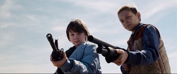 Movie still from “Cop Car” (2015), directed by Jon Watts – A boy and a woman holding guns in their hands; Medium shot, Low angle