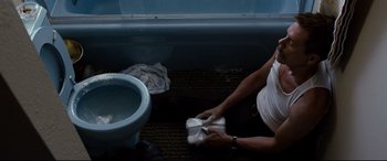 Movie still from “Cop Car” (2015), directed by Jon Watts – A person sitting on the floor next to a toilet; Medium shot, Overhead angle