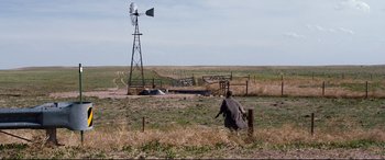 Movie still from “Cop Car” (2015), directed by Jon Watts – A person is sitting in a field near a windmill; Extreme Wide shot, High angle