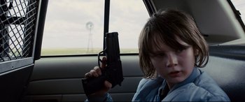 Movie still from “Cop Car” (2015), directed by Jon Watts – A young boy holding a gun in the back seat of a car; Close Up shot, Over the shoulder angle