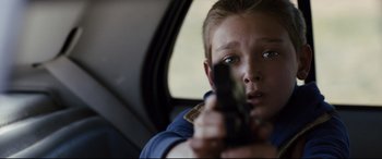Movie still from “Cop Car” (2015), directed by Jon Watts – A young boy holding a gun while sitting in a car; Close Up shot, Over the shoulder angle