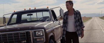Movie still from “Cop Car” (2015), directed by Jon Watts – A man standing in front of an old truck; Medium shot, Low angle