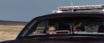 Movie still from “Cop Car” (2015), directed by Jon Watts – A young boy in the back of a police car looking out of the window; Medium shot, Low angle