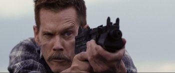 Movie still from “Cop Car” (2015), directed by Jon Watts – A person holding a gun; Close Up shot, Over the shoulder angle