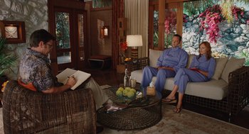 Movie still from “Couples Retreat” (2009), directed by Peter Billingsley – A man sitting on top of a white couch in a living room; Wide shot, High angle