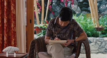 Movie still from “Couples Retreat” (2009), directed by Peter Billingsley – A man sitting in a chair writing on a piece of paper; Medium shot, High angle