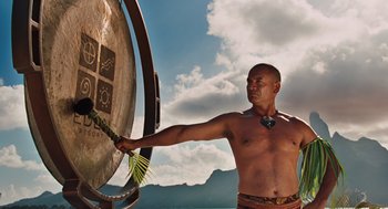 Movie still from “Couples Retreat” (2009), directed by Peter Billingsley – A man is playing a gong in the sky; Medium shot, Low angle
