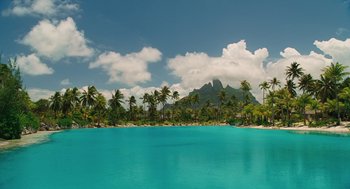 Movie still from “Couples Retreat” (2009), directed by Peter Billingsley – A body of water surrounded by palm trees and mountains; Extreme Wide shot, High angle
