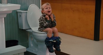 Movie still from “Couples Retreat” (2009), directed by Peter Billingsley – A little boy sitting on top of a white toilet seat; Medium shot, High angle