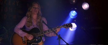Movie still from “Coyote Ugly” (2000), directed by David McNally – A woman holding a guitar in front of a microphone on a stage; Medium shot, Low angle