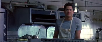 Movie still from “Coyote Ugly” (2000), directed by David McNally – A man in an apron standing in front of an oven; Medium shot, Low angle