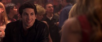 Movie still from “Coyote Ugly” (2000), directed by David McNally – A group of people in a room with a man smiling; Close Up shot, Over the shoulder angle