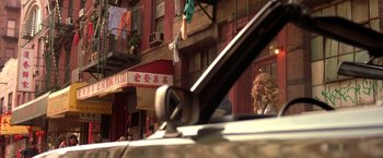Movie still from “Coyote Ugly” (2000), directed by David McNally – A woman sitting in the back of a white car in front of a building; Wide shot, Low angle