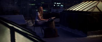 Movie still from “Coyote Ugly” (2000), directed by David McNally – A woman sitting on top of a chair on top of a building; Wide shot, High angle