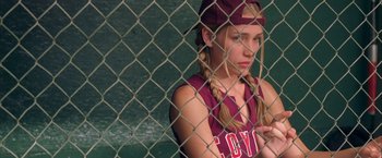 Movie still from “Coyote Ugly” (2000), directed by David McNally – A girl in a baseball uniform sitting in front of a chain link fence; Close Up shot, Low angle
