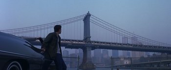 Movie still from “Coyote Ugly” (2000), directed by David McNally – A man walking on a bench in front of a bridge; Wide shot, Low angle