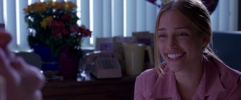 Movie still from “Coyote Ugly” (2000), directed by David McNally – A young woman smiles while sitting in front of a phone; Close Up shot, Over the shoulder angle