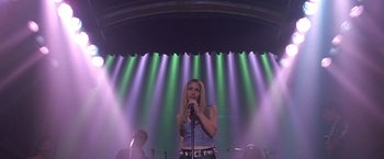 Movie still from “Coyote Ugly” (2000), directed by David McNally – A woman holding a microphone while standing in front of an audience; Wide shot, Low angle