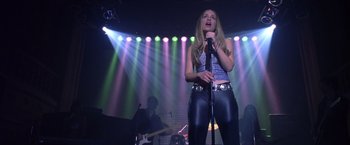 Movie still from “Coyote Ugly” (2000), directed by David McNally – A woman is singing into a microphone on stage; Medium shot, Low angle