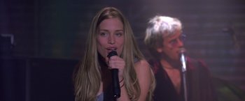 Movie still from “Coyote Ugly” (2000), directed by David McNally – A beautiful young woman holding a microphone while standing in front of a man; Close Up shot, Over the shoulder angle
