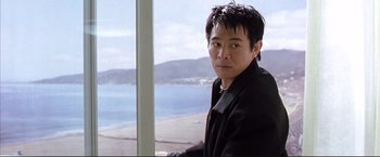 Movie still from “Cradle 2 the Grave” (2003), directed by Andrzej Bartkowiak – A man in a black jacket looking out of a window; Medium shot, Low angle