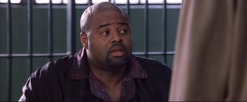 Movie still from “Cradle 2 the Grave” (2003), directed by Andrzej Bartkowiak – A man in a black shirt is sitting in front of bars; Close Up shot, High angle