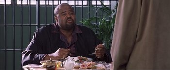 Movie still from “Cradle 2 the Grave” (2003), directed by Andrzej Bartkowiak – A man sitting at a table with a plate of food in front of him; Medium shot, High angle