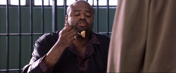Movie still from “Cradle 2 the Grave” (2003), directed by Andrzej Bartkowiak – A man eating a piece of pizza in a jail cell; Medium shot, High angle