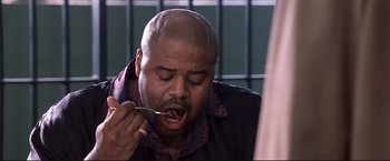Movie still from “Cradle 2 the Grave” (2003), directed by Andrzej Bartkowiak – A man with a shaved head is holding a spoon in his mouth; Close Up shot, High angle