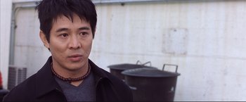 Movie still from “Cradle 2 the Grave” (2003), directed by Andrzej Bartkowiak – A man wearing a black jacket standing in front of a grill; Close Up shot, Over the shoulder angle
