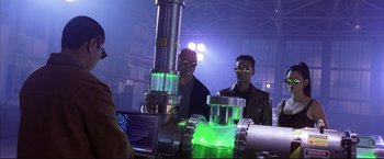 Movie still from “Cradle 2 the Grave” (2003), directed by Andrzej Bartkowiak – Two men are standing next to a machine with green lights; Medium shot, Low angle