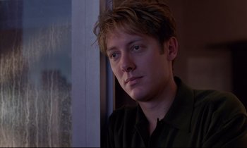 Movie still from “Crash” (1996), directed by David Cronenberg – A young man is sitting in front of a window; Close Up shot, Over the shoulder angle