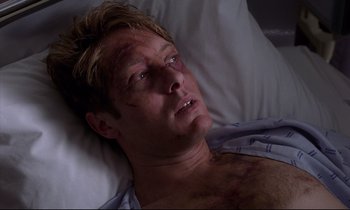 Movie still from “Crash” (1996), directed by David Cronenberg – A person laying in a hospital bed with bruises; Close Up shot, Overhead angle