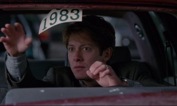 Movie still from “Crash” (1996), directed by David Cronenberg – A man sitting in the back seat of a car with the number 1 9 8 3 on it; Close Up shot, Low angle