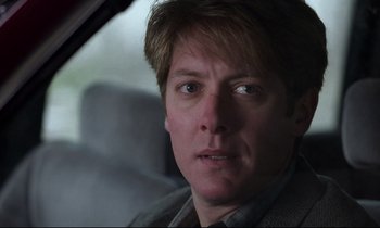 Movie still from “Crash” (1996), directed by David Cronenberg – A person sitting in a car looking at the camera; Close Up shot, Over the shoulder angle