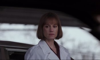 Movie still from “Crash” (1996), directed by David Cronenberg – A woman in a white lab coat standing in front of a car; Close Up shot, Over the shoulder angle