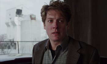 Movie still from “Crash” (1996), directed by David Cronenberg – A man in a jacket and a shirt is looking at the camera; Close Up shot, Over the shoulder angle