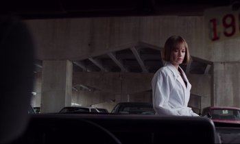 Movie still from “Crash” (1996), directed by David Cronenberg – A woman in a white lab coat standing next to a car; Medium shot, Low angle