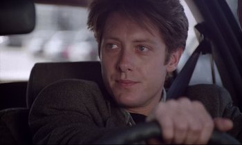 Movie still from “Crash” (1996), directed by David Cronenberg – A person sitting in a car holding a steering wheel; Close Up shot, Low angle