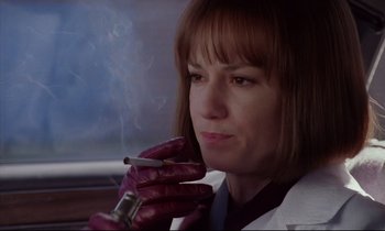Movie still from “Crash” (1996), directed by David Cronenberg – A woman smoking a cigarette while sitting in a car; Close Up shot, Low angle