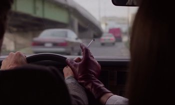 Movie still from “Crash” (1996), directed by David Cronenberg – A person wearing gloves and holding a cigarette while driving a car; Close Up shot, Low angle