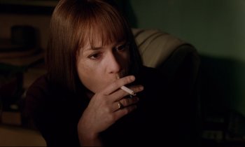 Movie still from “Crash” (1996), directed by David Cronenberg – A woman smoking a cigarette while sitting on a couch; Close Up shot, High angle