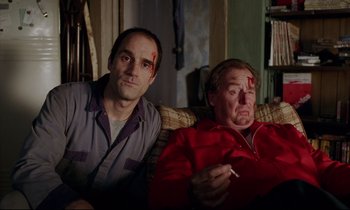 Movie still from “Crash” (1996), directed by David Cronenberg – Two men sitting next to each other on a couch; Medium shot, High angle