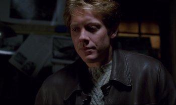 Movie still from “Crash” (1996), directed by David Cronenberg – A man wearing a brown leather jacket looking to his left; Close Up shot, Over the shoulder angle