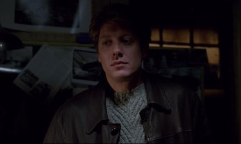 Movie still from “Crash” (1996), directed by David Cronenberg – A man in a brown leather jacket and a sweater; Close Up shot, Over the shoulder angle