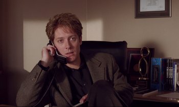 Movie still from “Crash” (1996), directed by David Cronenberg – A man sitting in a chair talking on a phone; Medium shot, High angle
