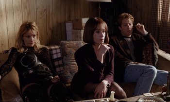 Movie still from “Crash” (1996), directed by David Cronenberg – A group of people sitting around a living room together; Medium shot, Over the shoulder angle
